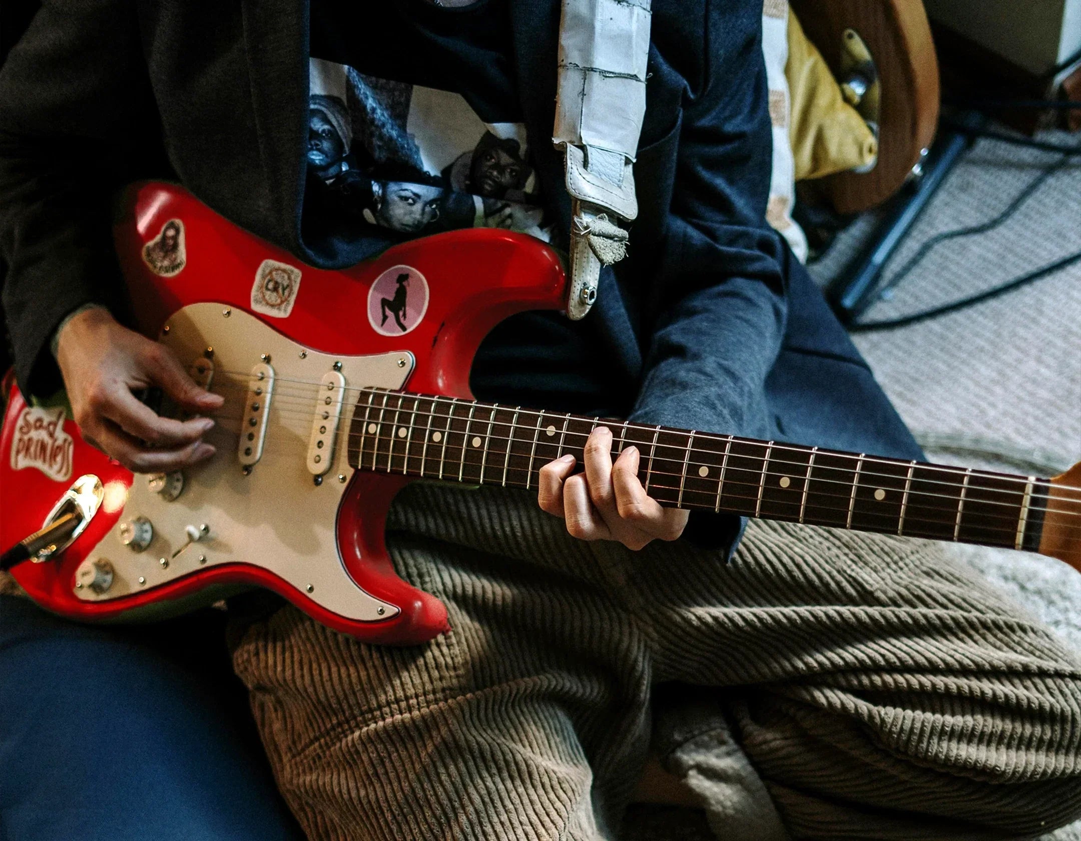 Musician playing red Fender Stratocaster sitting down.