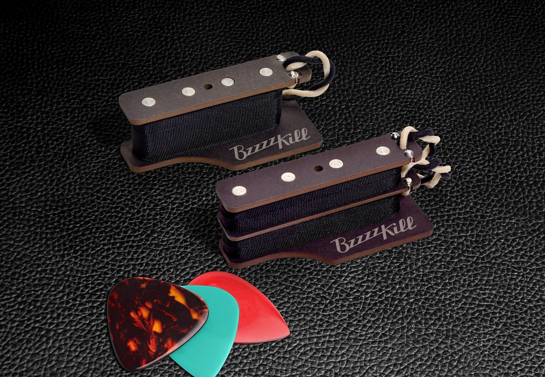 The BzzzzKill Dual and Single Layer devices for eliminating Fender Stratocaster 60 cycle hum in all pickup selector positions, on black guitar case with guitar picks.