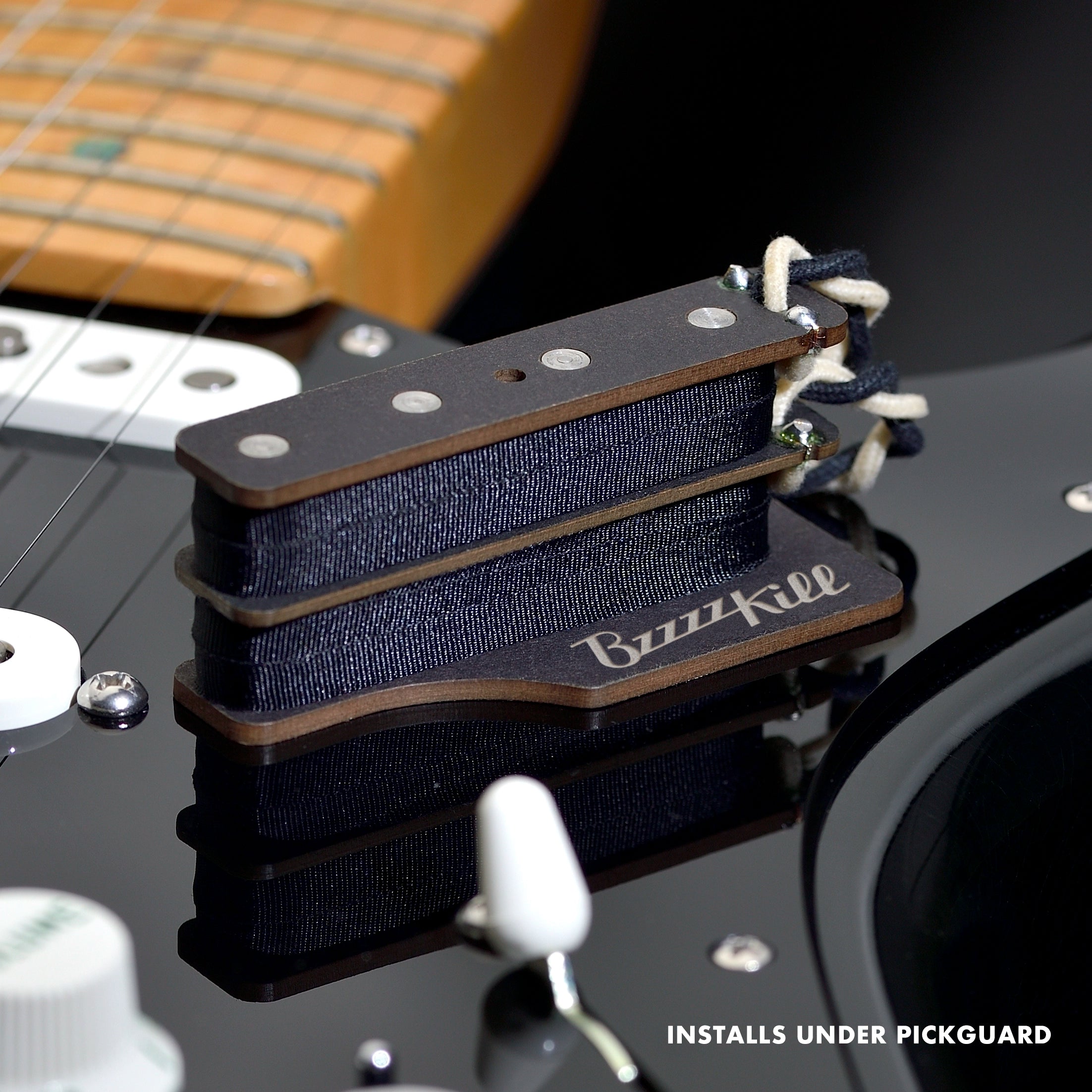 The BzzzzKill Dual Layer device for eliminating Fender Stratocaster 60 cycle hum in all pickup selector positions. Sitting on black Stratocaster. With text "Installs under pickguard".