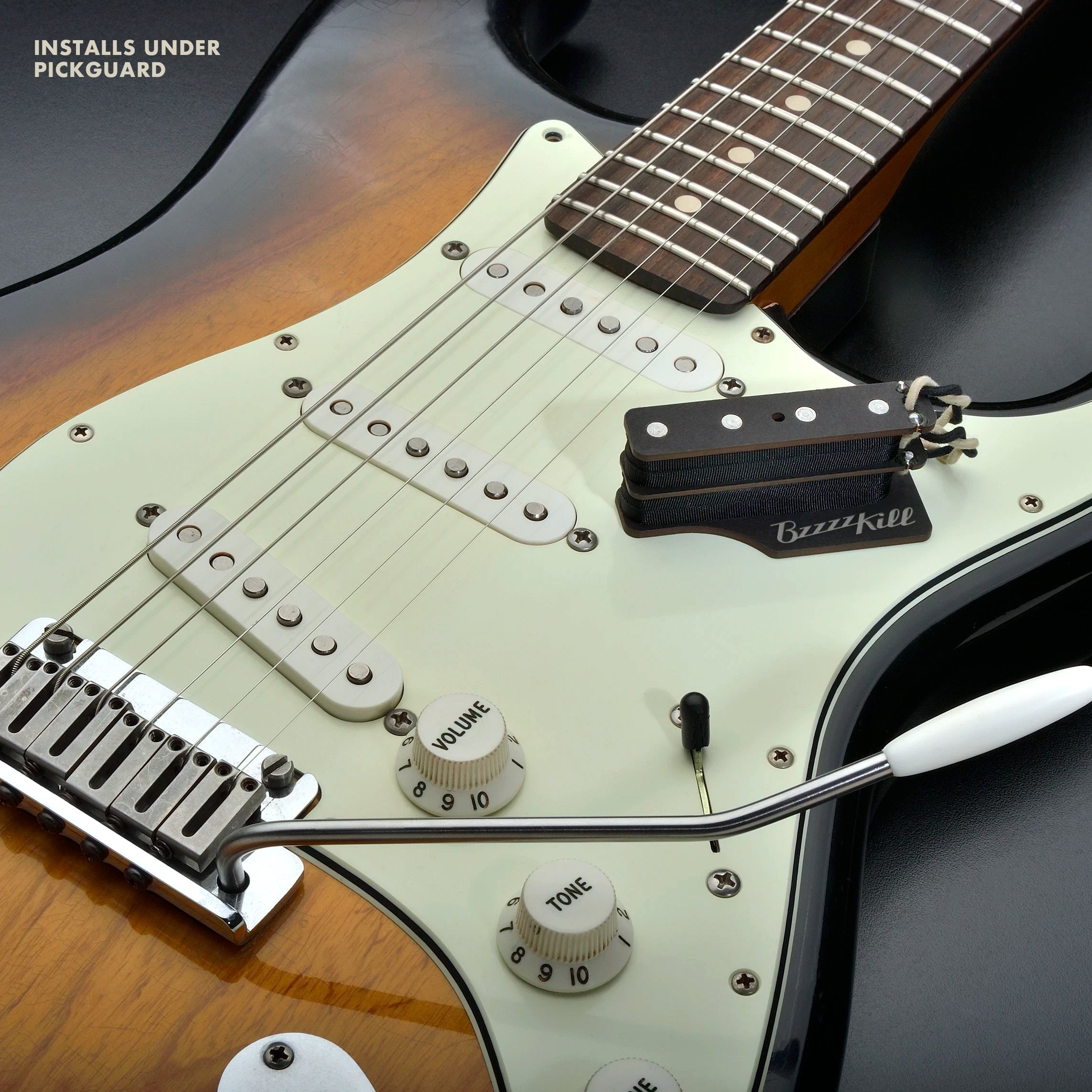 The BzzzzKill Dual Layer device for eliminating Fender Stratocaster 60 cycle hum in all pickup selector positions. Sitting on sunburst Stratocaster. With text "Installs under pickguard".