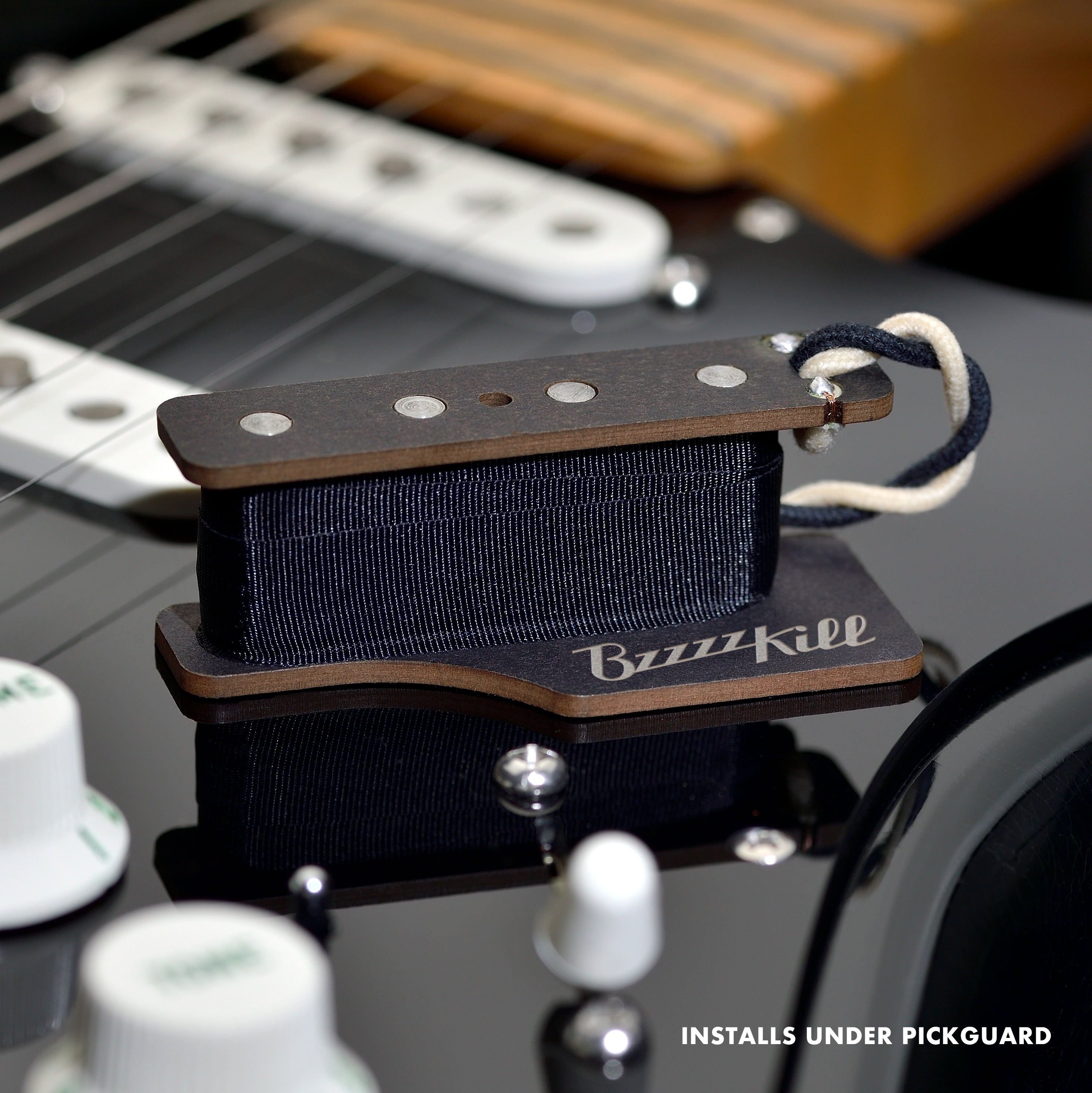 The BzzzzKill Single Layer device for eliminating Fender Stratocaster 60 cycle hum in all pickup selector positions. Sitting on black Stratocaster. With text "Installs under pickguard".