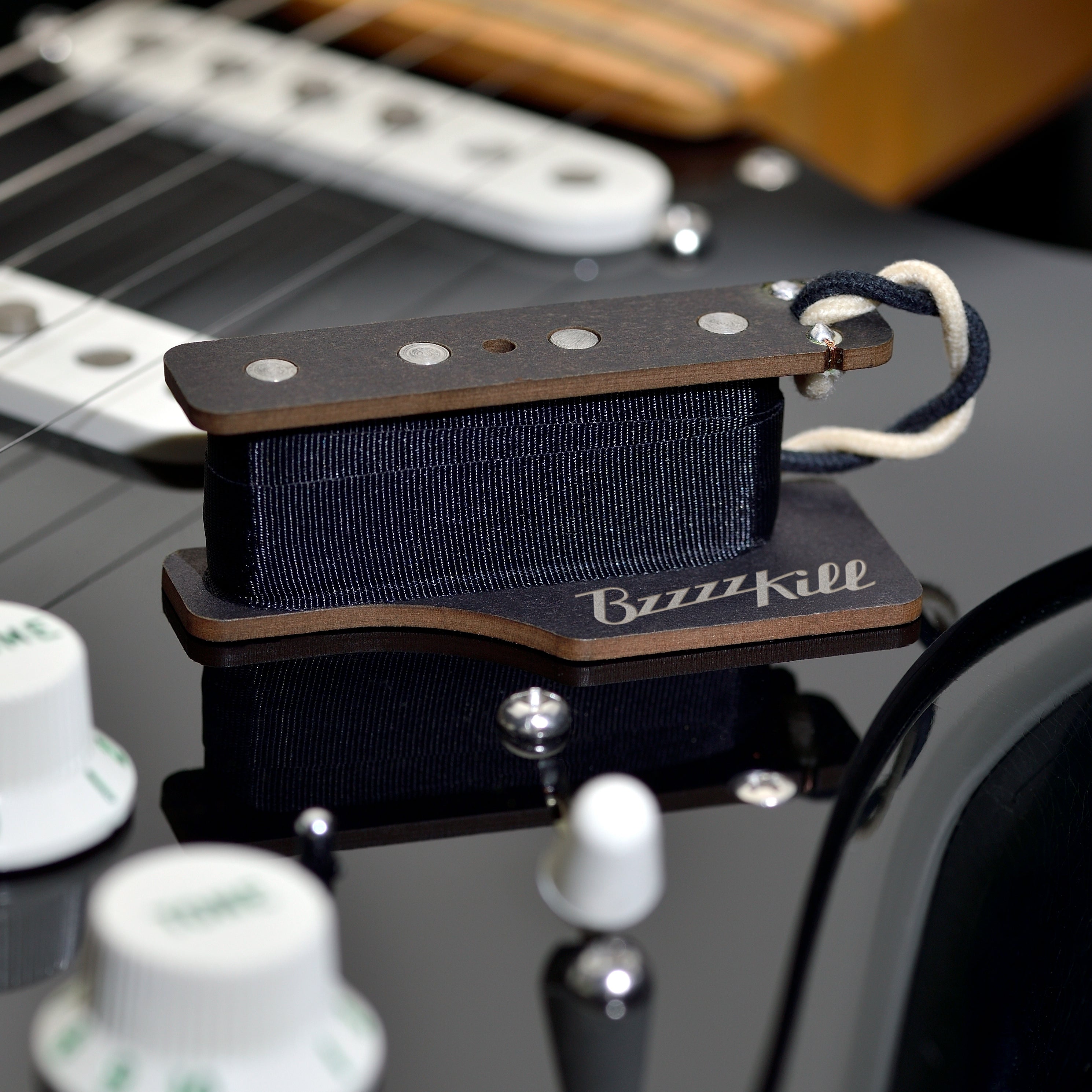 The BzzzzKill Single Layer device for eliminating Fender Stratocaster 60 cycle hum in all pickup selector positions. Sitting on black Stratocaster.