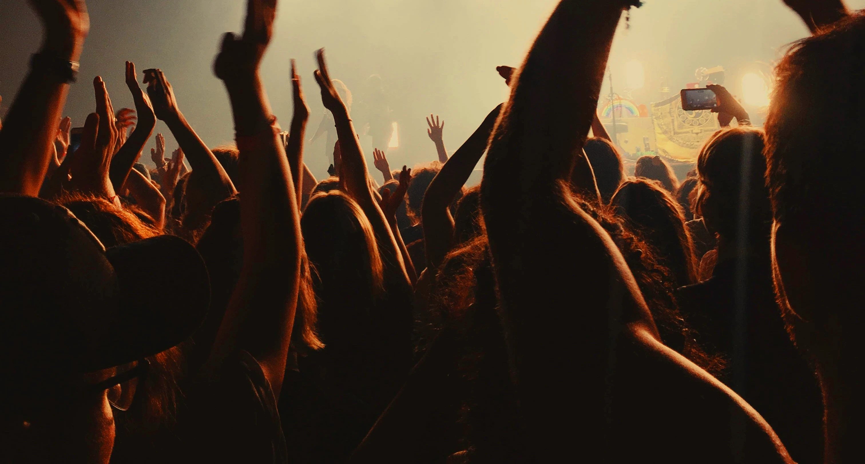Concert crowd with arms raised, with dramatic lighting.