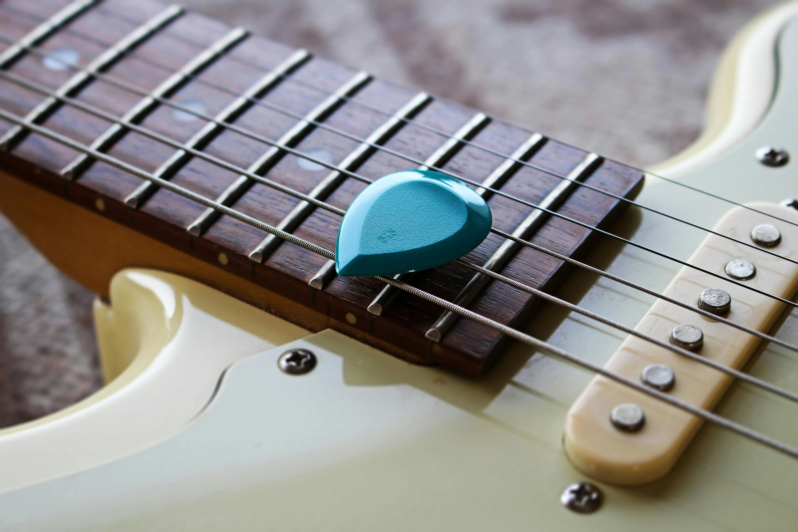 Close up of guitar pick resting on strings close to pickup of Olympic White Fender Stratocaster.