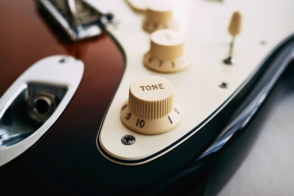 Close up of tone control knob on Fender Stratocaster with ivory pickguard.